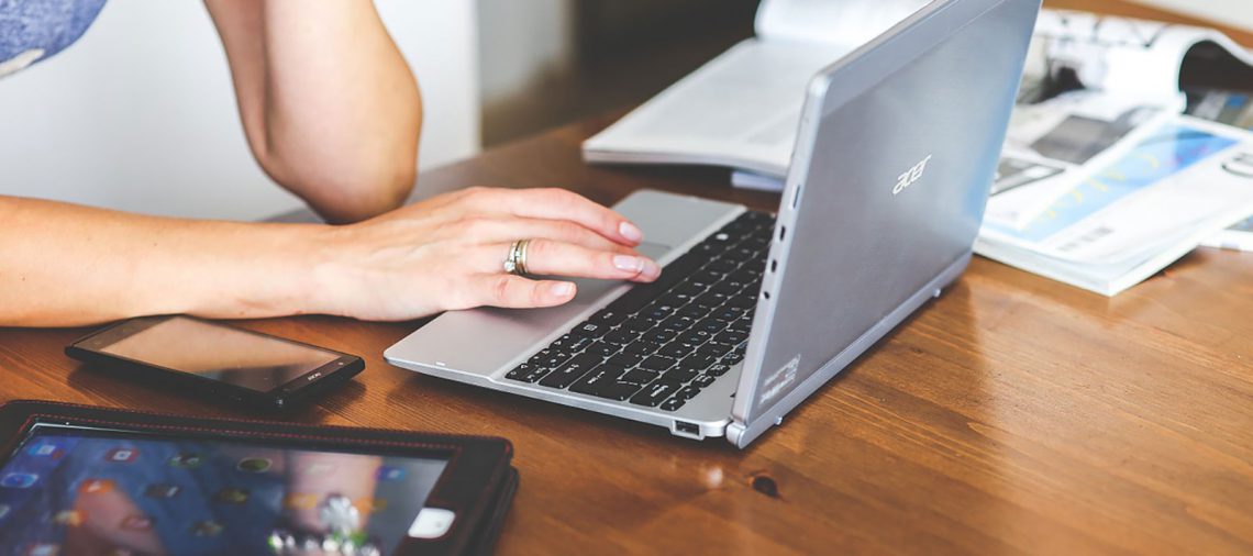Vrouw achter laptop met tablet en papieren