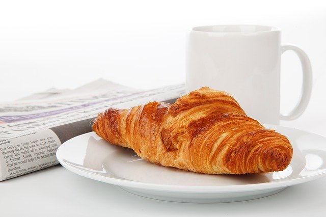 een kopje koffie, een croissant en een krant